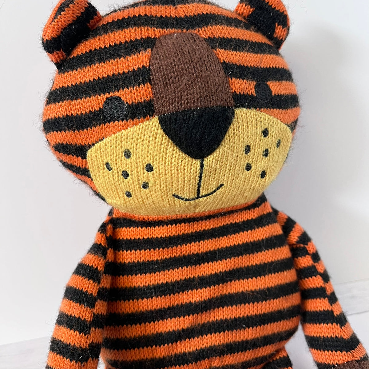 Knitted tiger toy with orange and black stripes on a white background