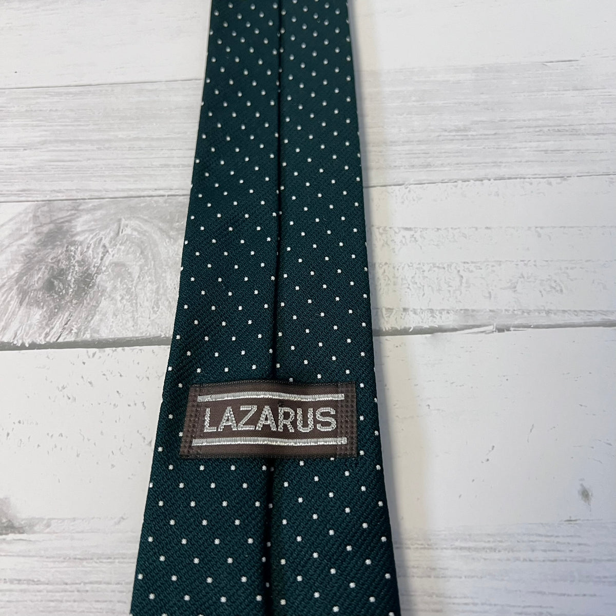 Green tie with white polka dots and 'Lazarus' label on a light wooden surface