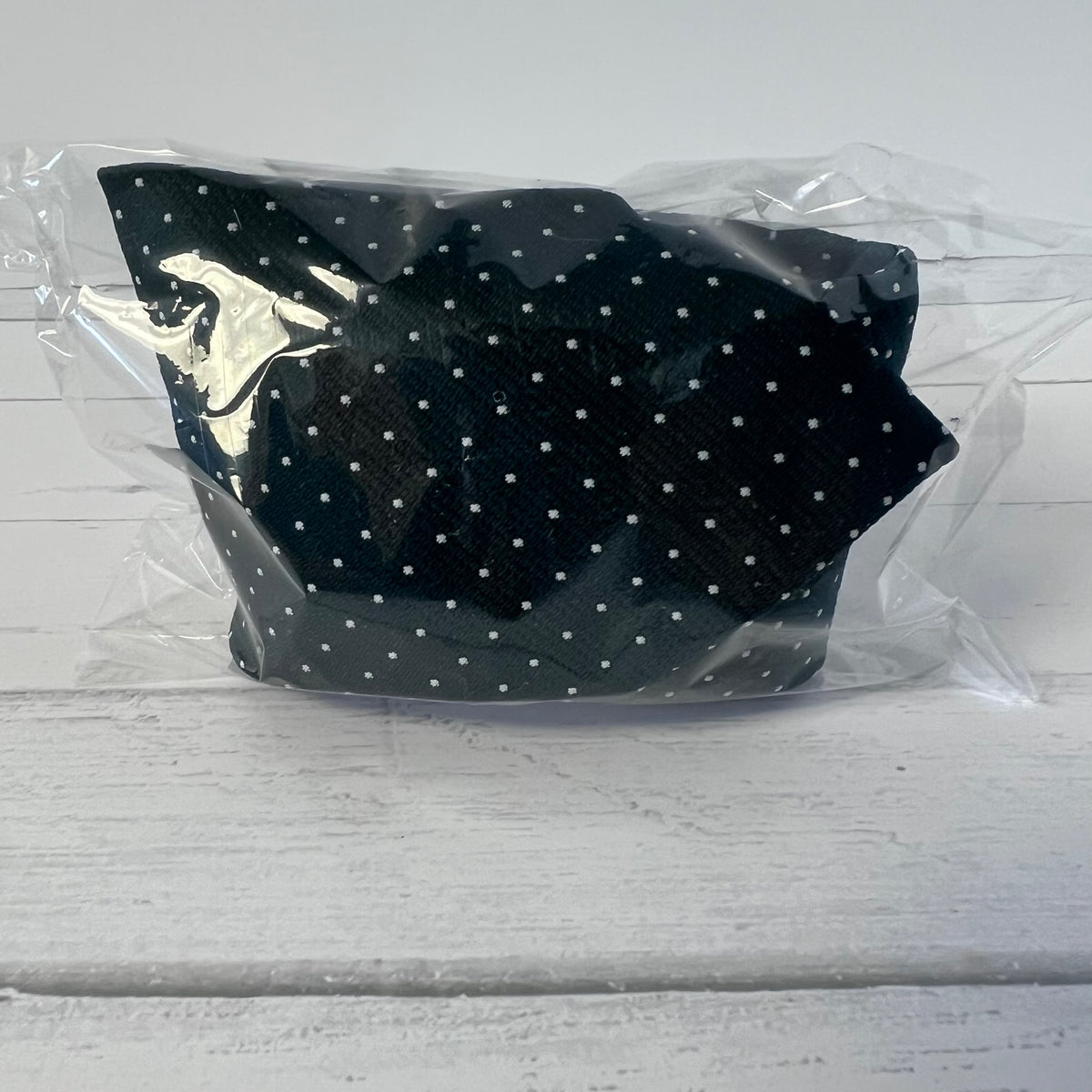 green polka dot tie with a silver logo in clear packaging on a light gray background
