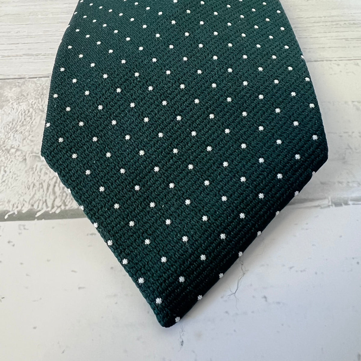 Dark green tie with white polka dots on a light gray surface