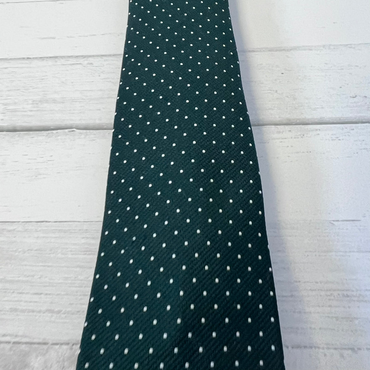 Green tie with white polka dots on a light wooden surface