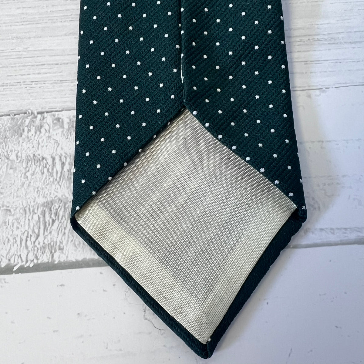 Dark green tie with white polka dots and matching pocket square on a light wooden surface