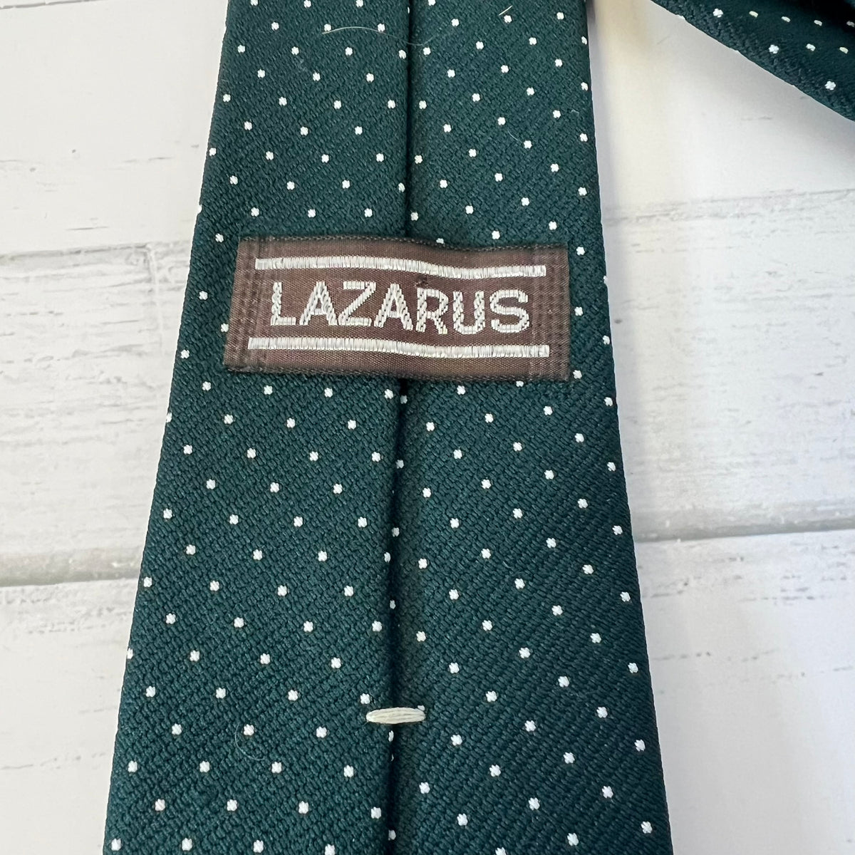 Green tie with white polka dots and 'Lazarus' label on a light wooden surface