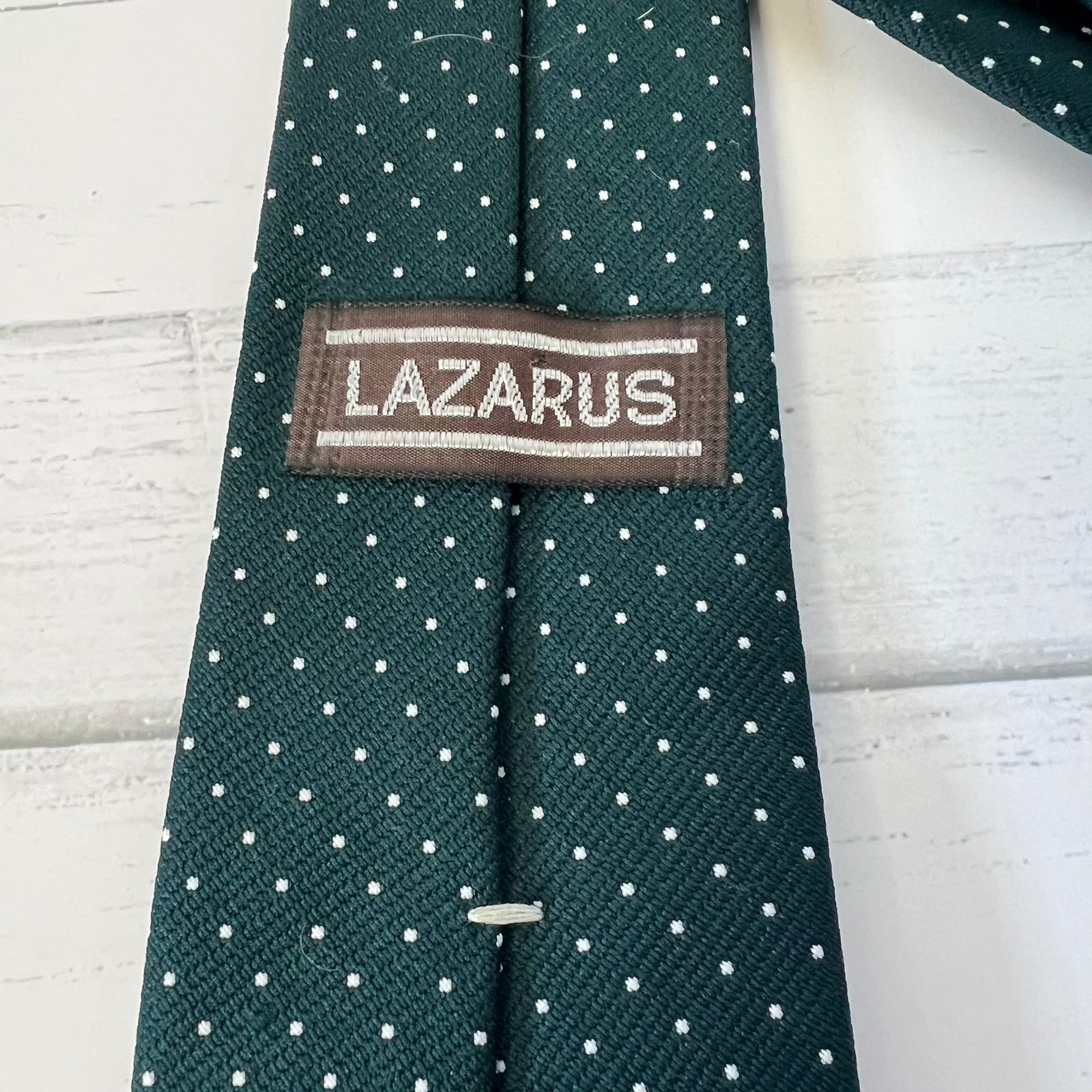 Green tie with white polka dots and 'Lazarus' label on a light wooden surface