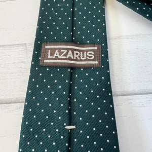 Green tie with white polka dots and 'Lazarus' label on a light wooden surface