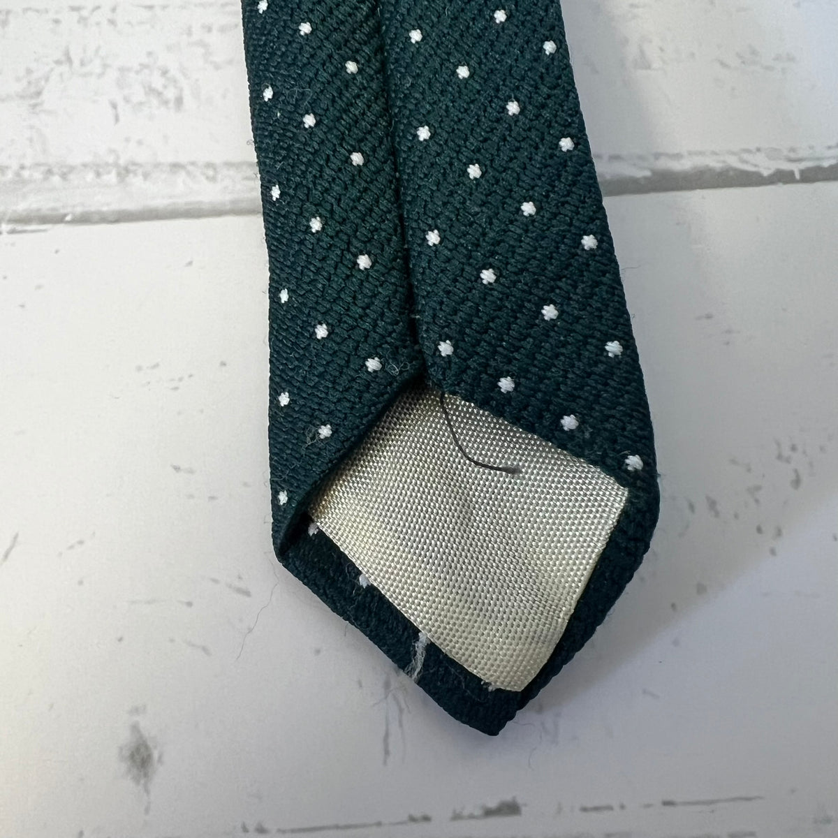 Dark green tie with white polka dots on a light gray surface