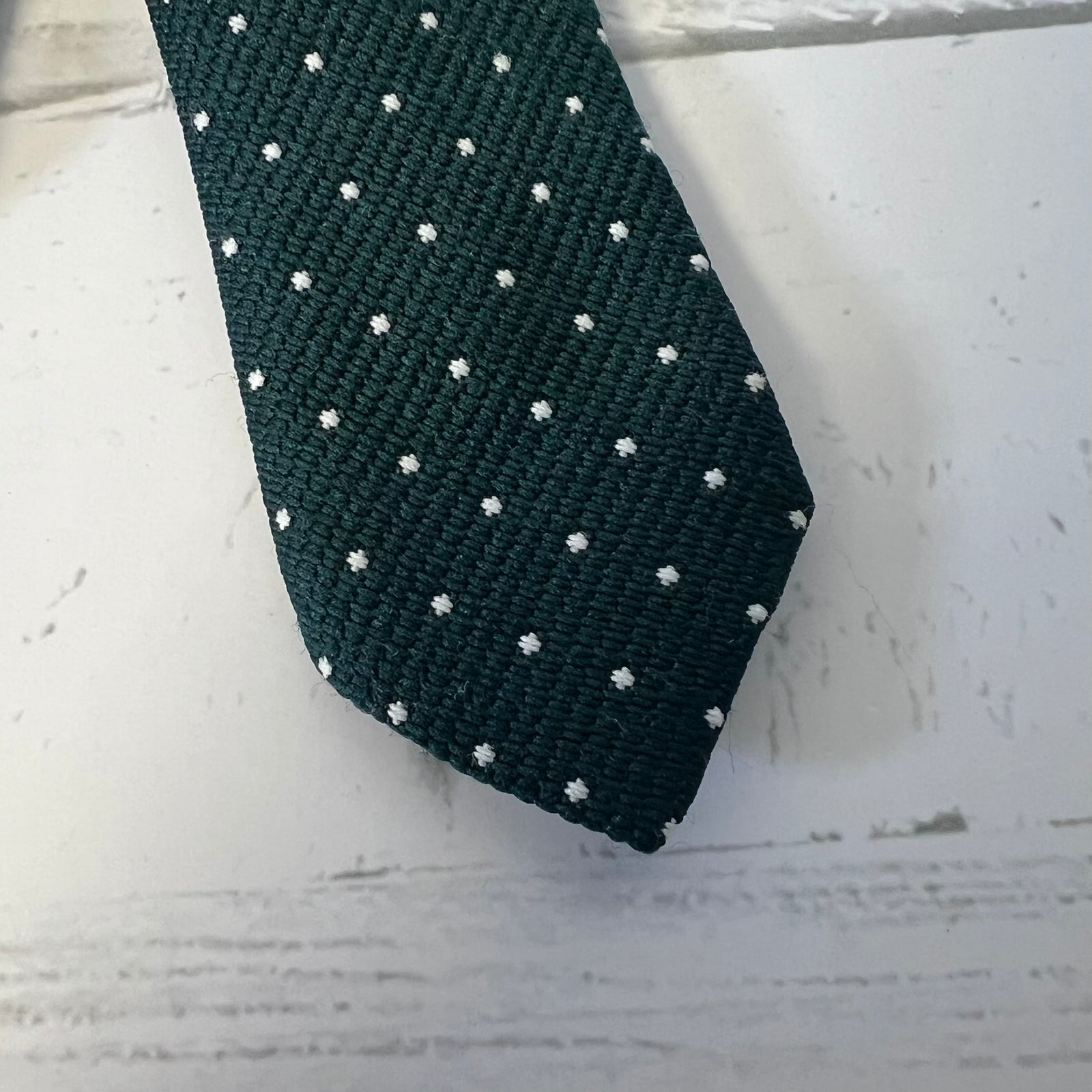 Dark green tie with white polka dots on a light wooden surface