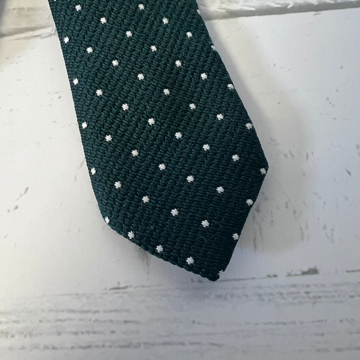 Dark green tie with white polka dots on a light wooden surface