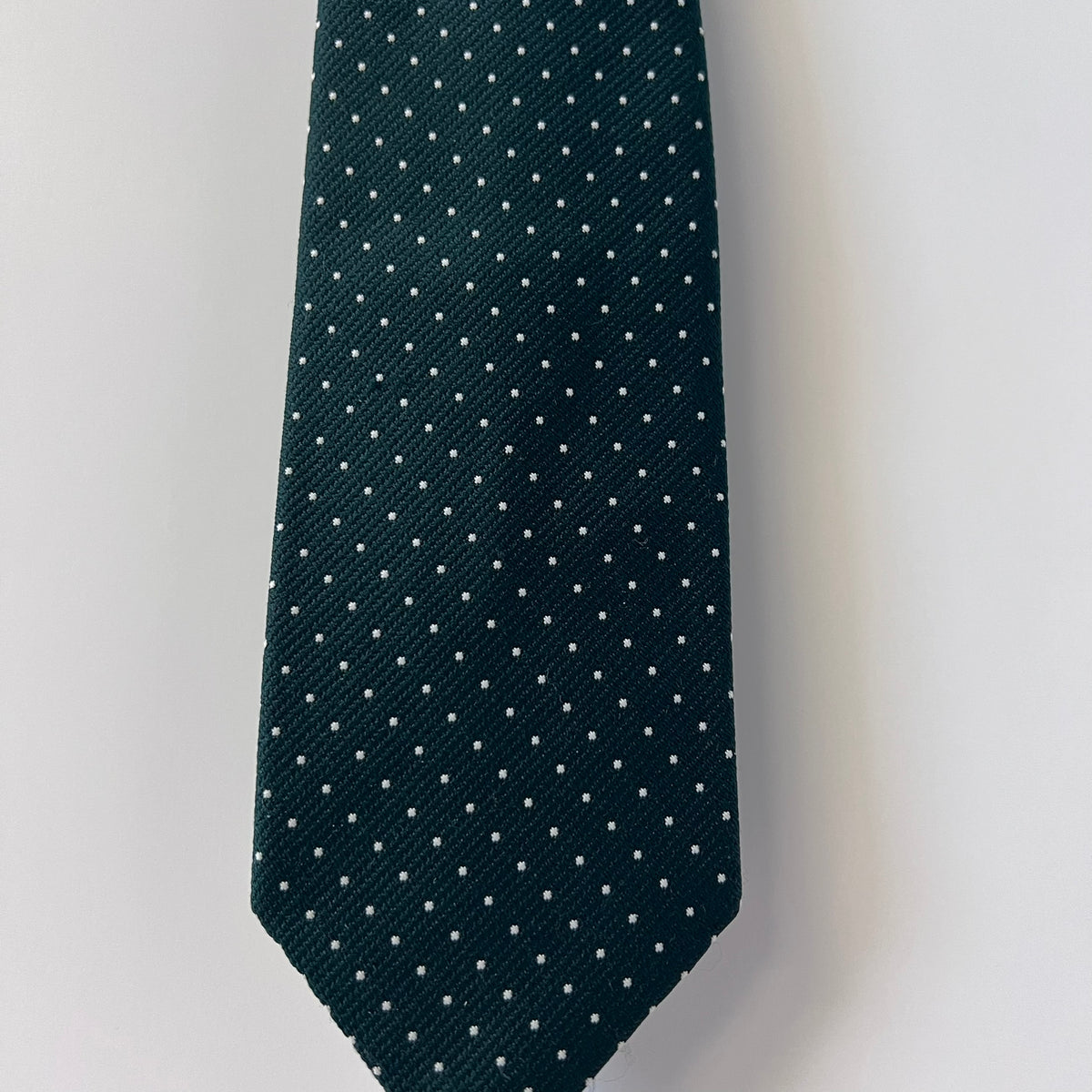 Dark green tie with white polka dots on a light gray background