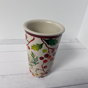 Decorative ceramic cup with holly design on a white wooden surface