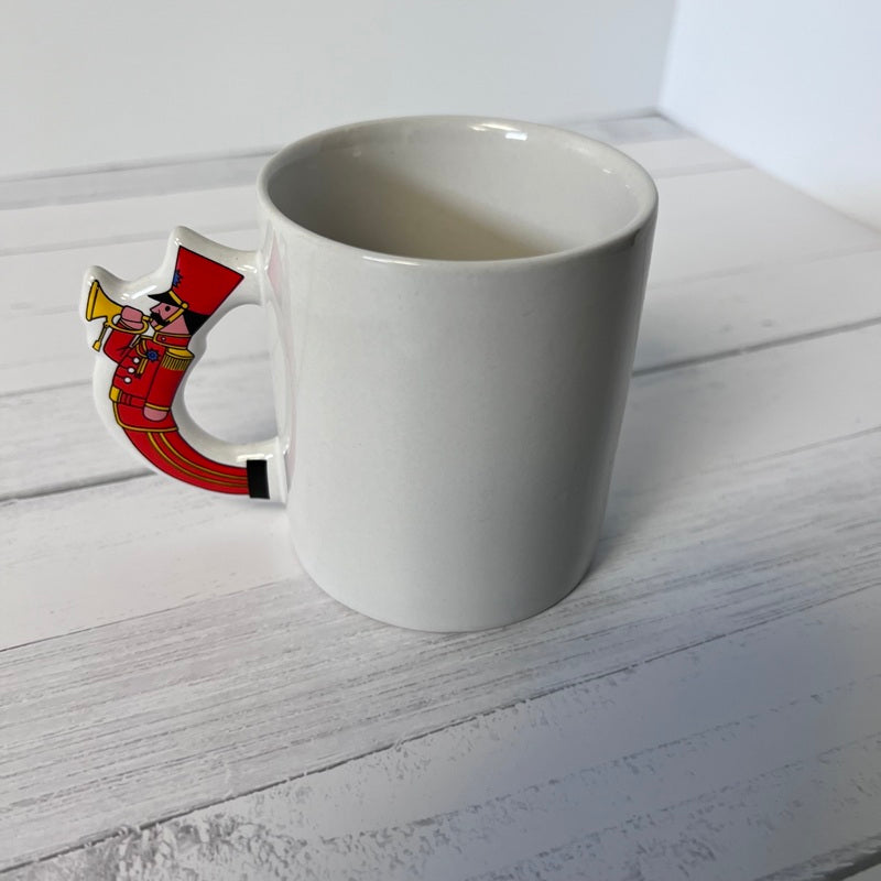 White mug with a decorative handle featuring a red and gold design on a white wooden surface.
