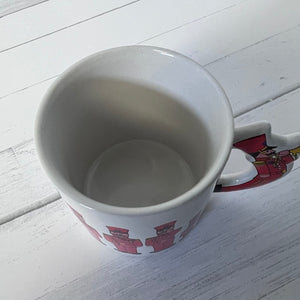 White mug with red and yellow design on a white wooden surface