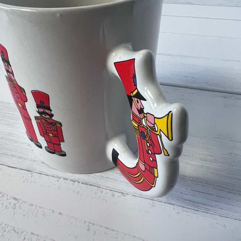 White mug with a decorative handle shaped like a nutcracker on a white wooden surface.