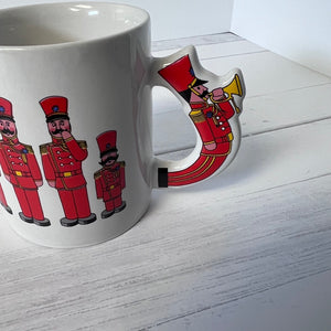 White mug with red nutcracker design on a white wooden surface