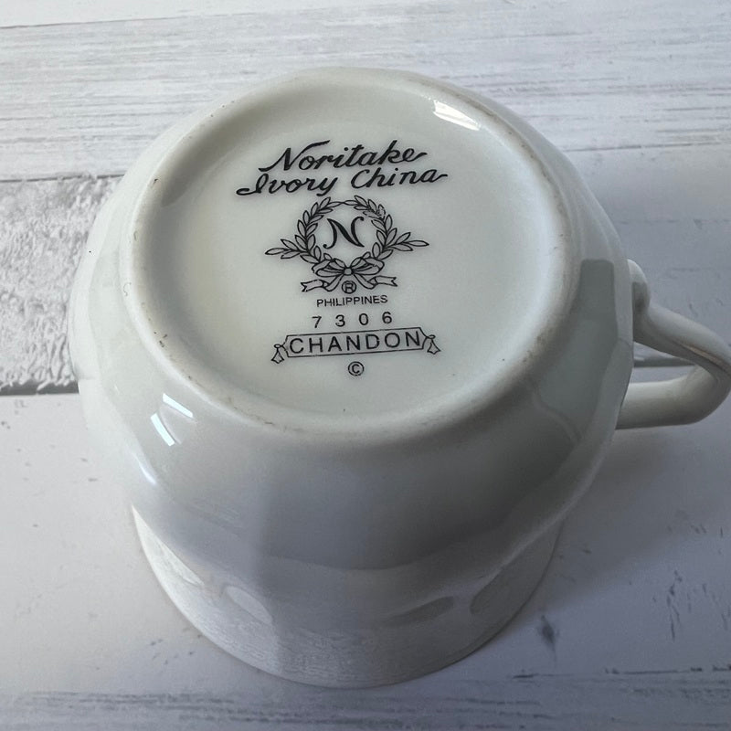 White ceramic cup with 'Noritake Ivory China' branding on a light wooden surface
