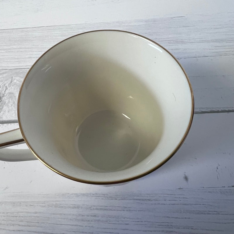 Empty beige mug with gold rim on a light wooden surface
