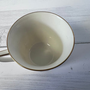 Empty beige mug with gold rim on a light wooden surface