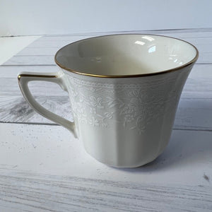 White ceramic mug with gold rim and intricate design on a light wooden surface