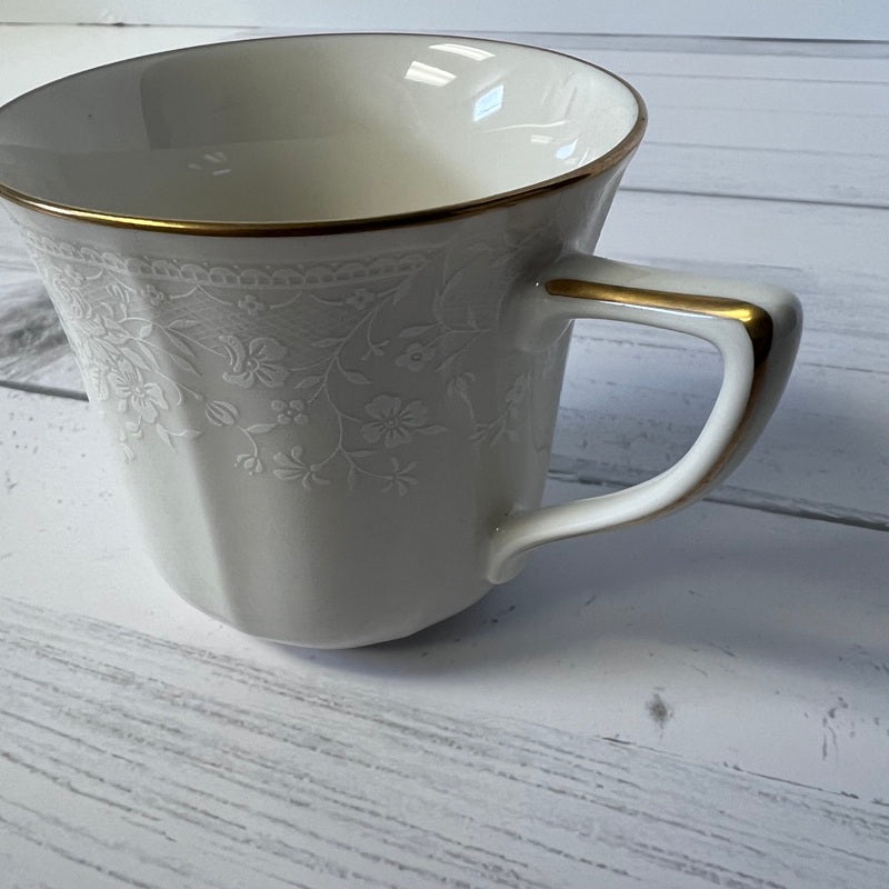 White mug with gold rim and handle on a light wooden surface