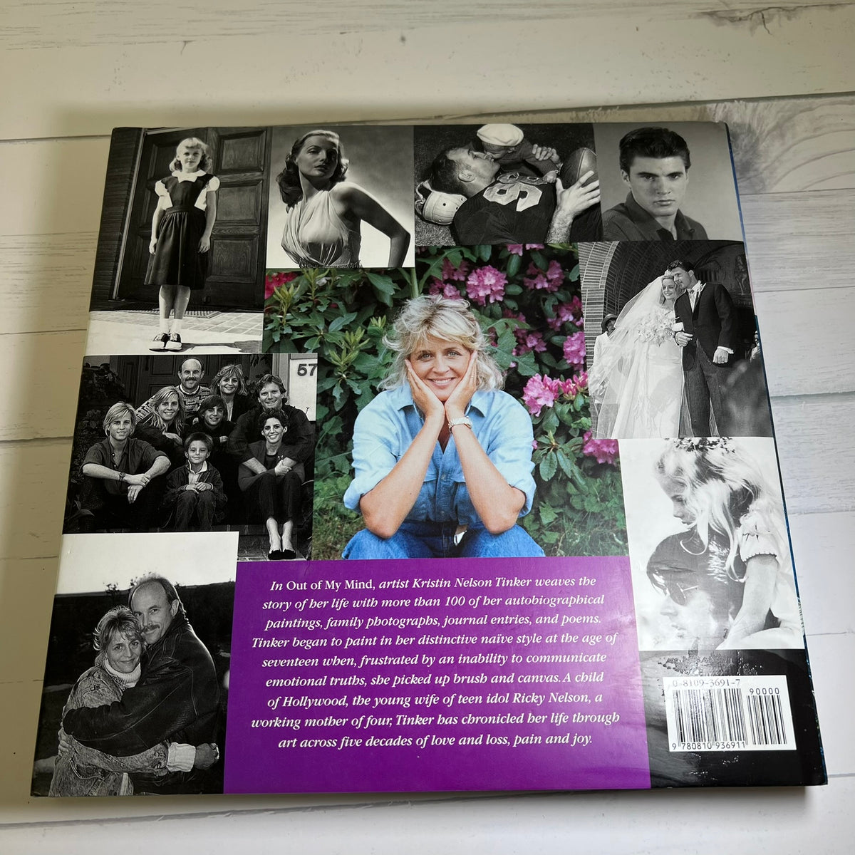 The back cover of a book titled 'In Out of My Mind' by artist Krutim Nikolai Tiber, displayed flat on a white wood background. The cover features a collage of black and white portraits of Tiber, a color portrait of her in a blue shirt, pink flowers, and a prominent purple text box at the bottom.