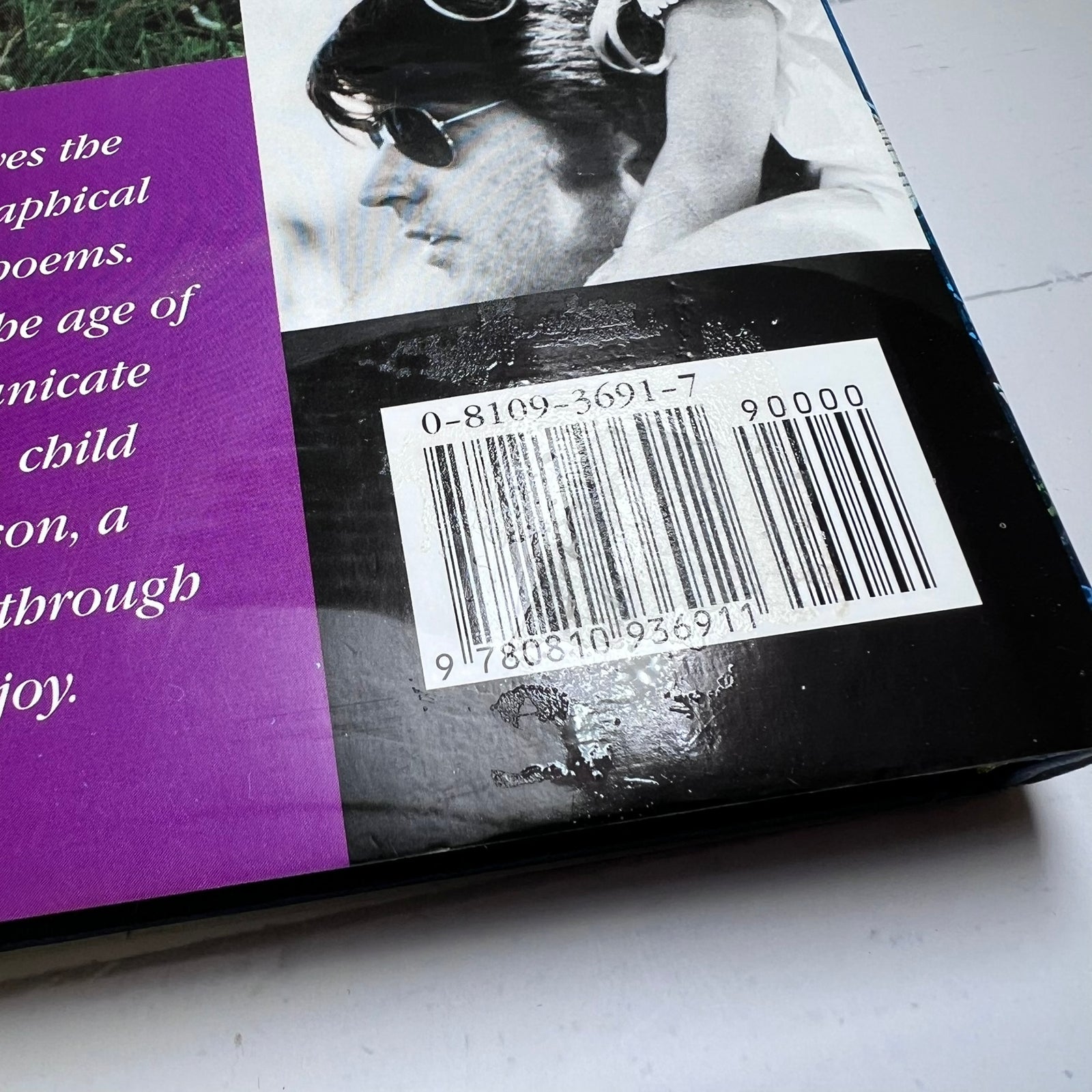 Close-up of a book cover showing a purple text panel on the left, a black-and-white portrait photo on the right, and a white barcode sticker over the center.
