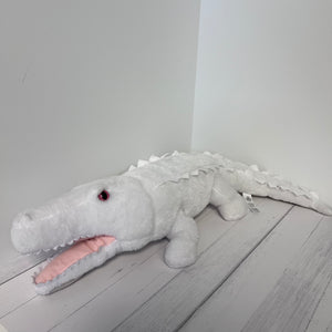 Plush toy alligator on a wooden floor with a white wall background