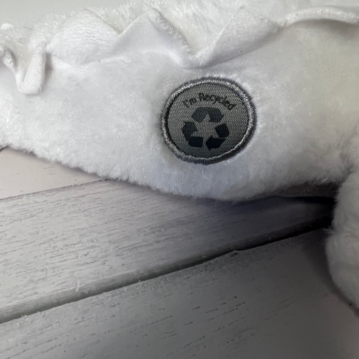 White plush toy with a recycling symbol label on a wooden surface