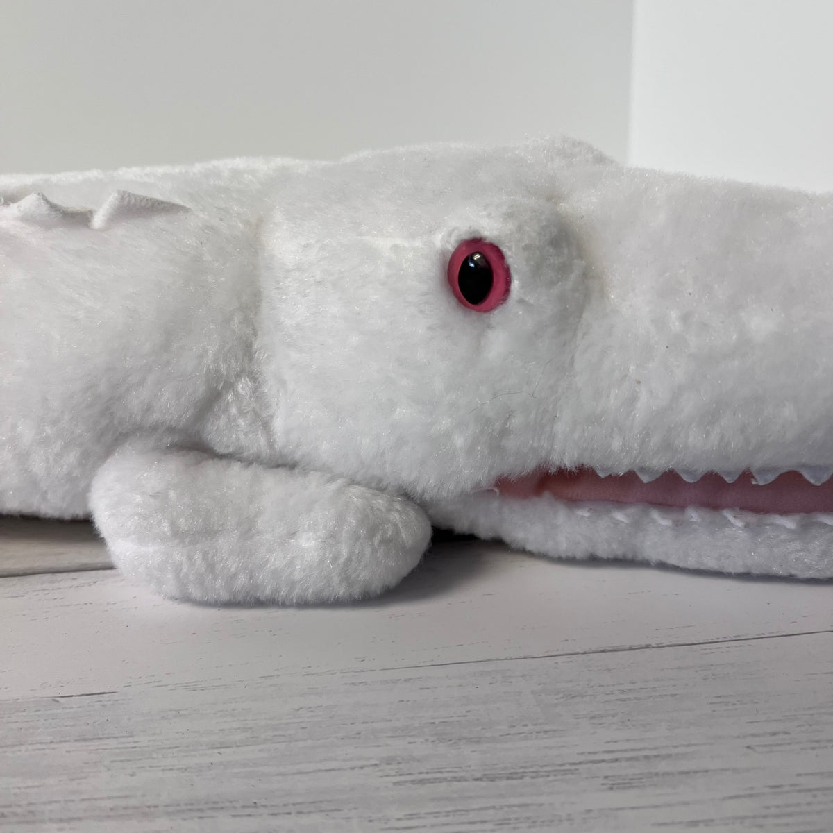 White plush shark toy with a red eye on a light wooden floor.