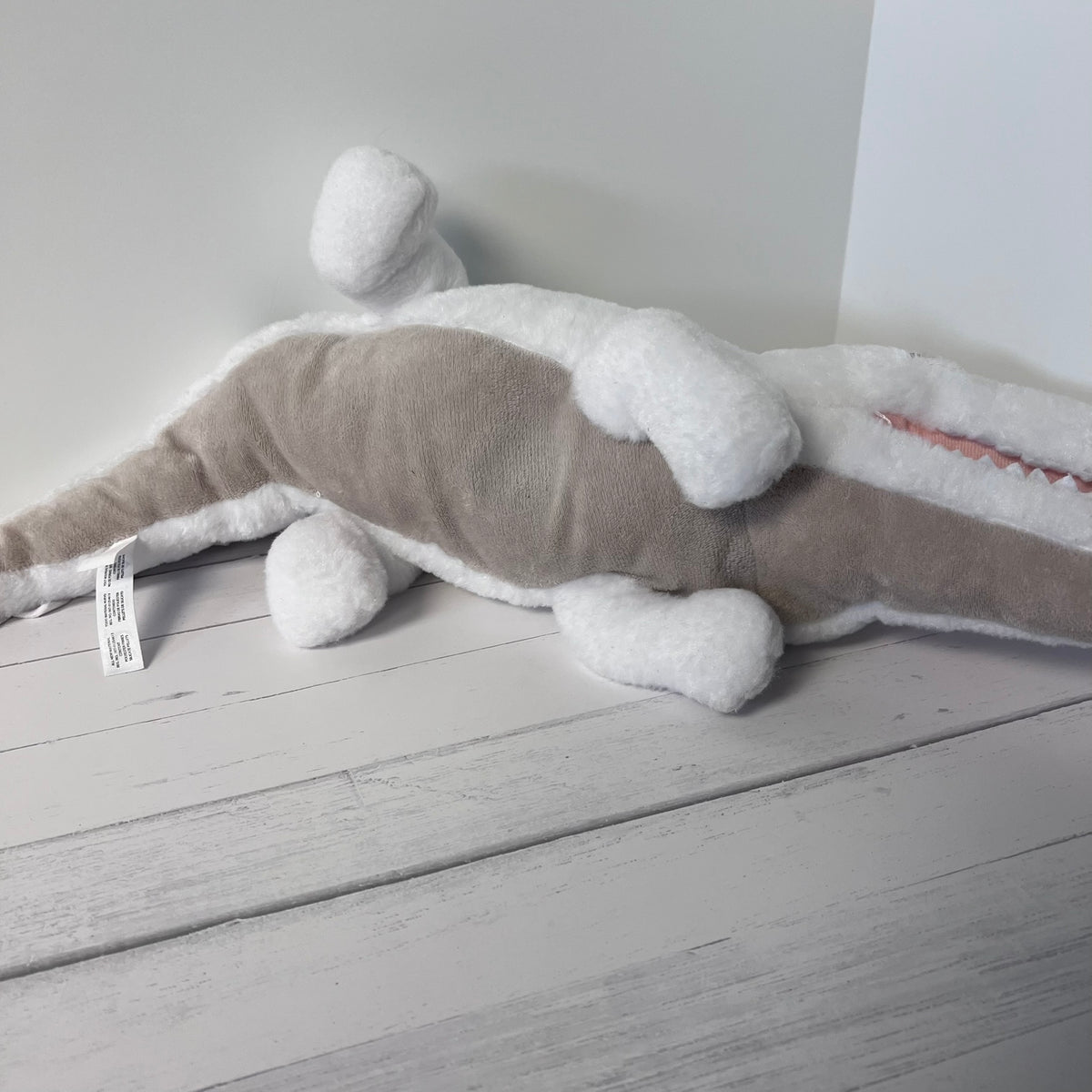 Plush toy shark on a light wooden floor with a white wall background