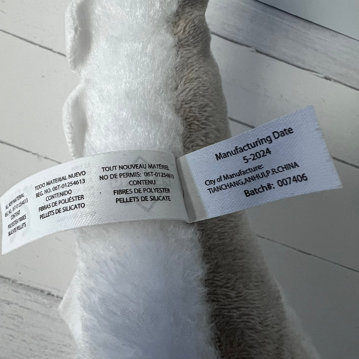 Plush toy with a label showing manufacturing details on a light wooden floor.