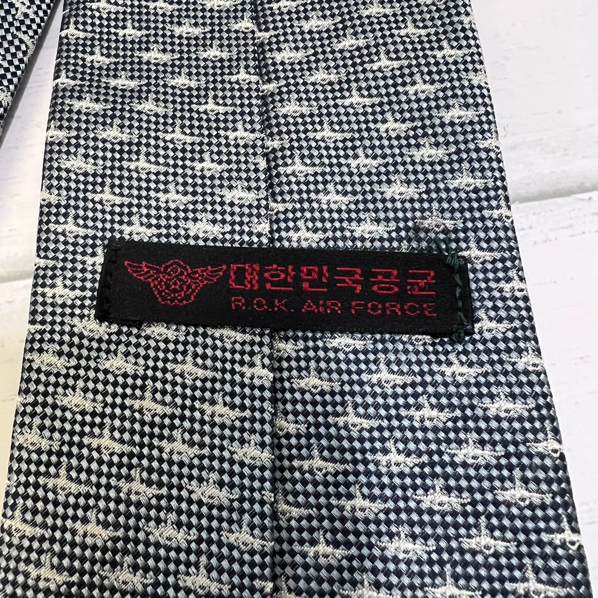 Black and white patterned tie with a label reading 'P.O.K. Air Force' on a light background