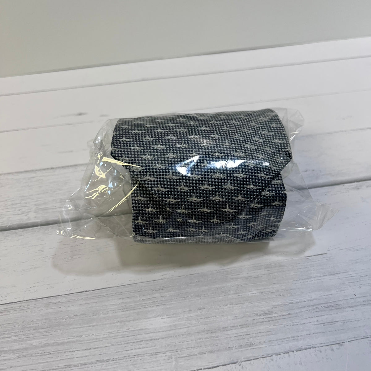 Black patterned fabric roll in clear plastic packaging on a light wooden surface