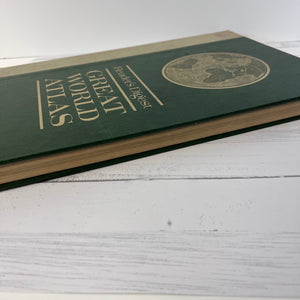 Green atlas book with gold text on a white wooden surface