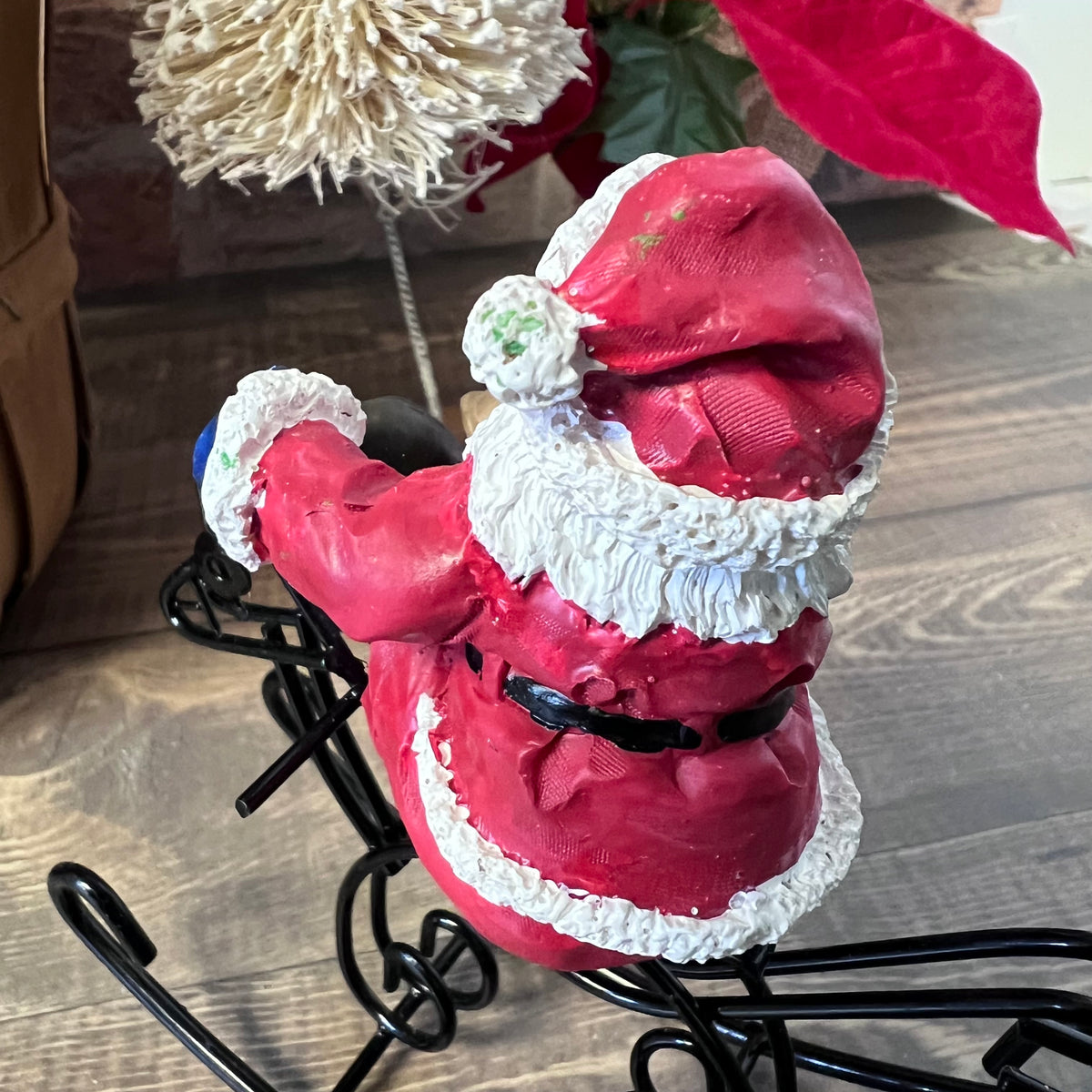 Red Santa Claus figurine with white trim on a black stand, surrounded by Christmas decorations.