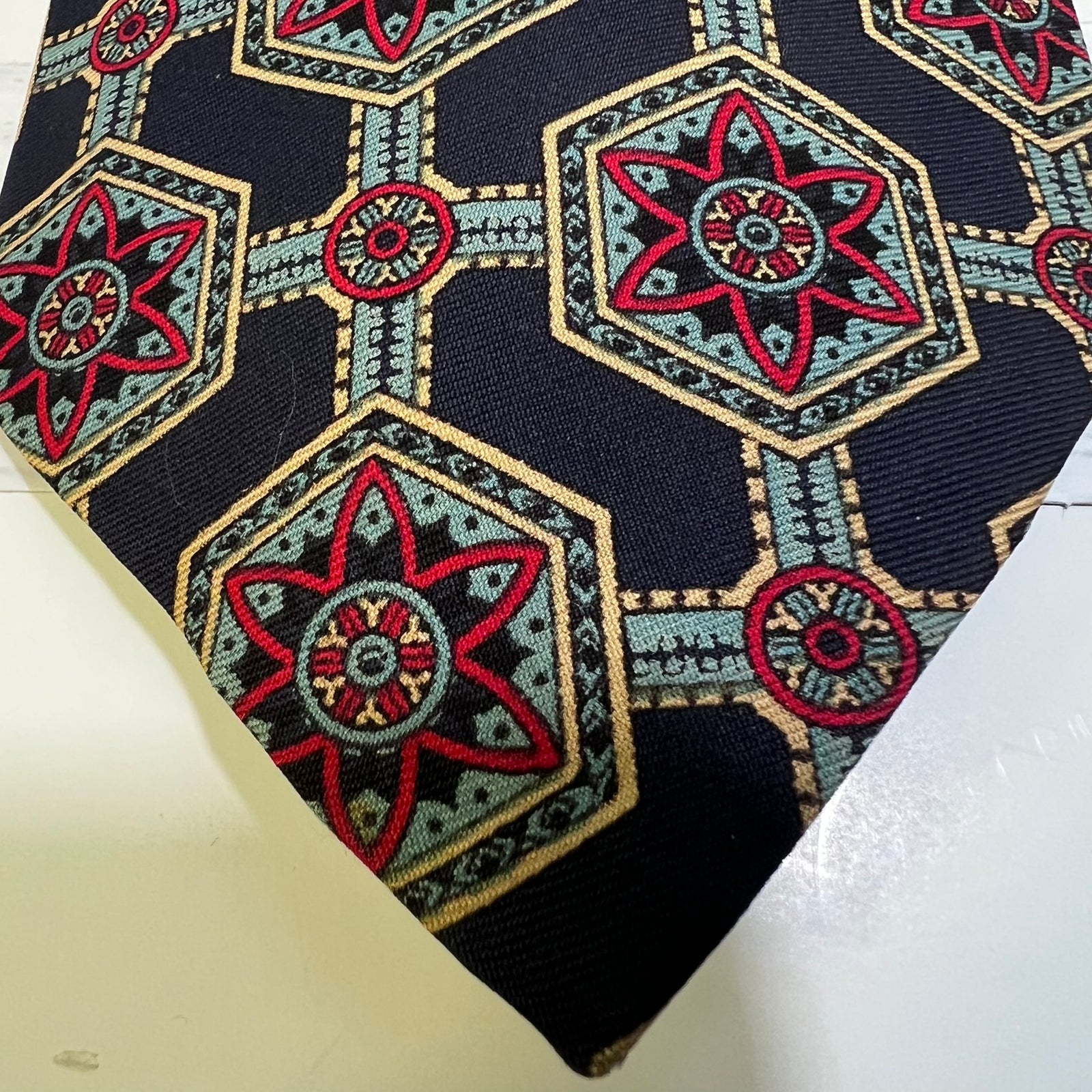 A close-up of a patterned necktie featuring a dark navy base with geometric and starburst motifs in red, beige, and light blue.