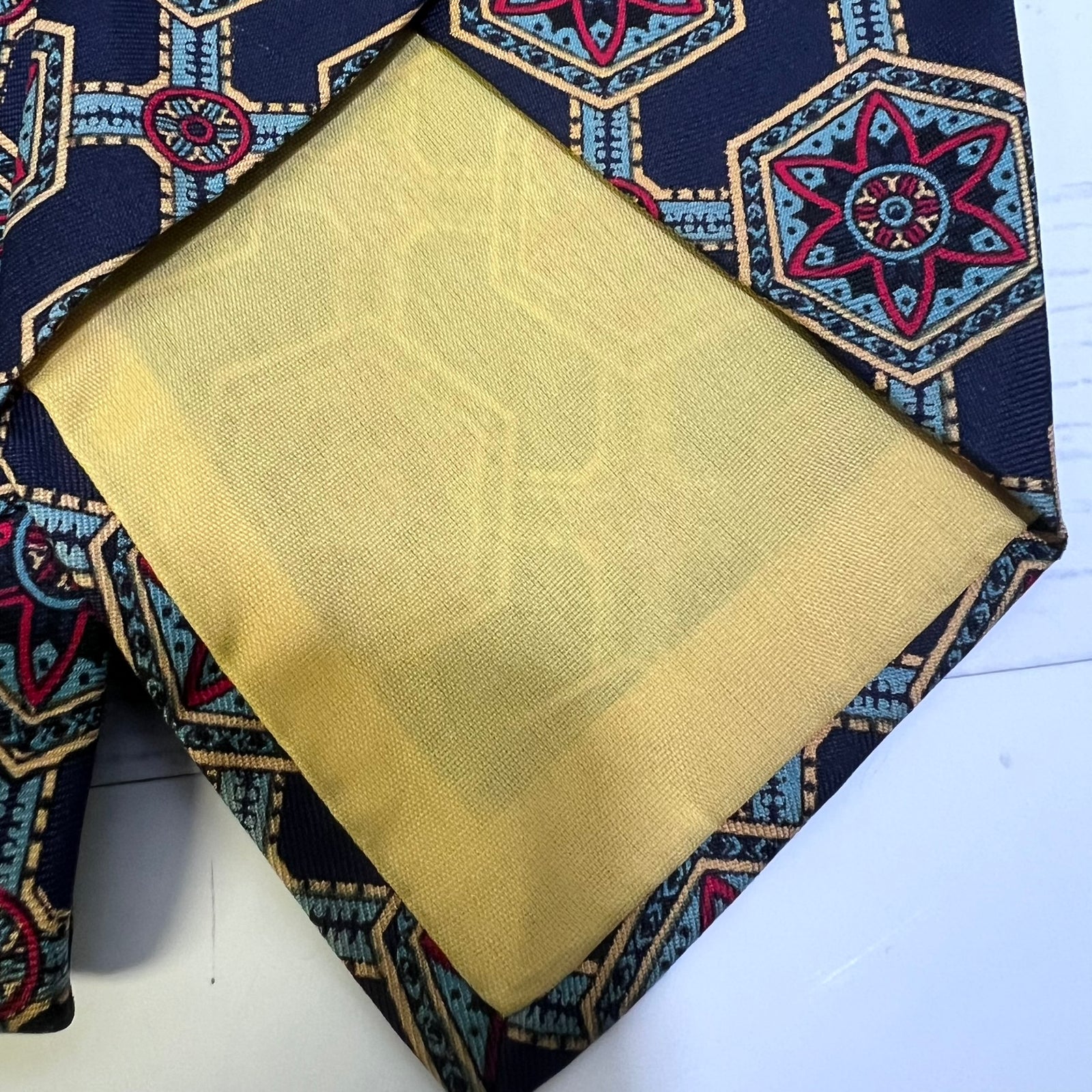 A folded necktie with a navy blue base and a colorful geometric pattern in red, blue, and gold, featuring a prominent yellow-gold satin neckband.