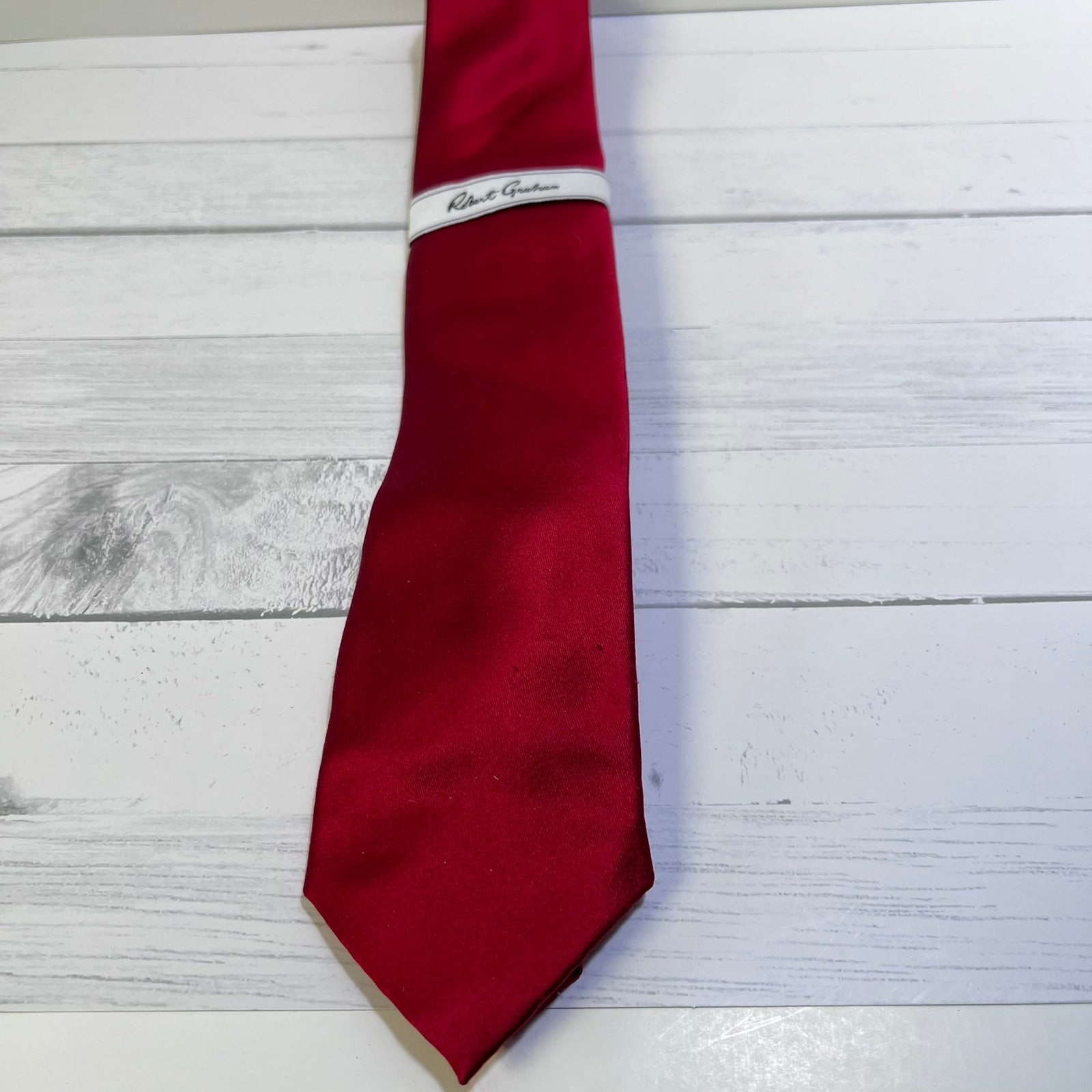 A red silk necktie with a white band inscribed with 'Robert Gordon' in black script, laid flat on a white wood plank background.