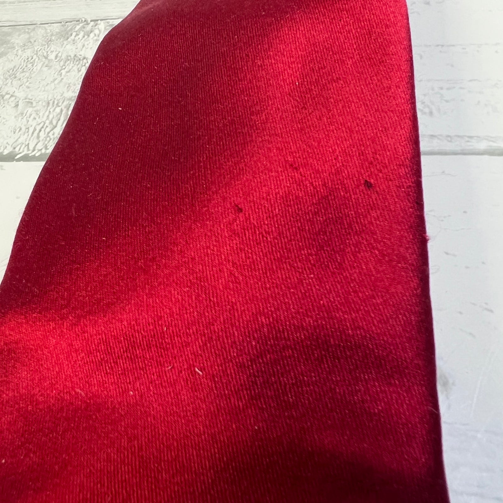 A close-up of a deep red fabric, likely velvet or velour, laid flat on a white wooden surface.