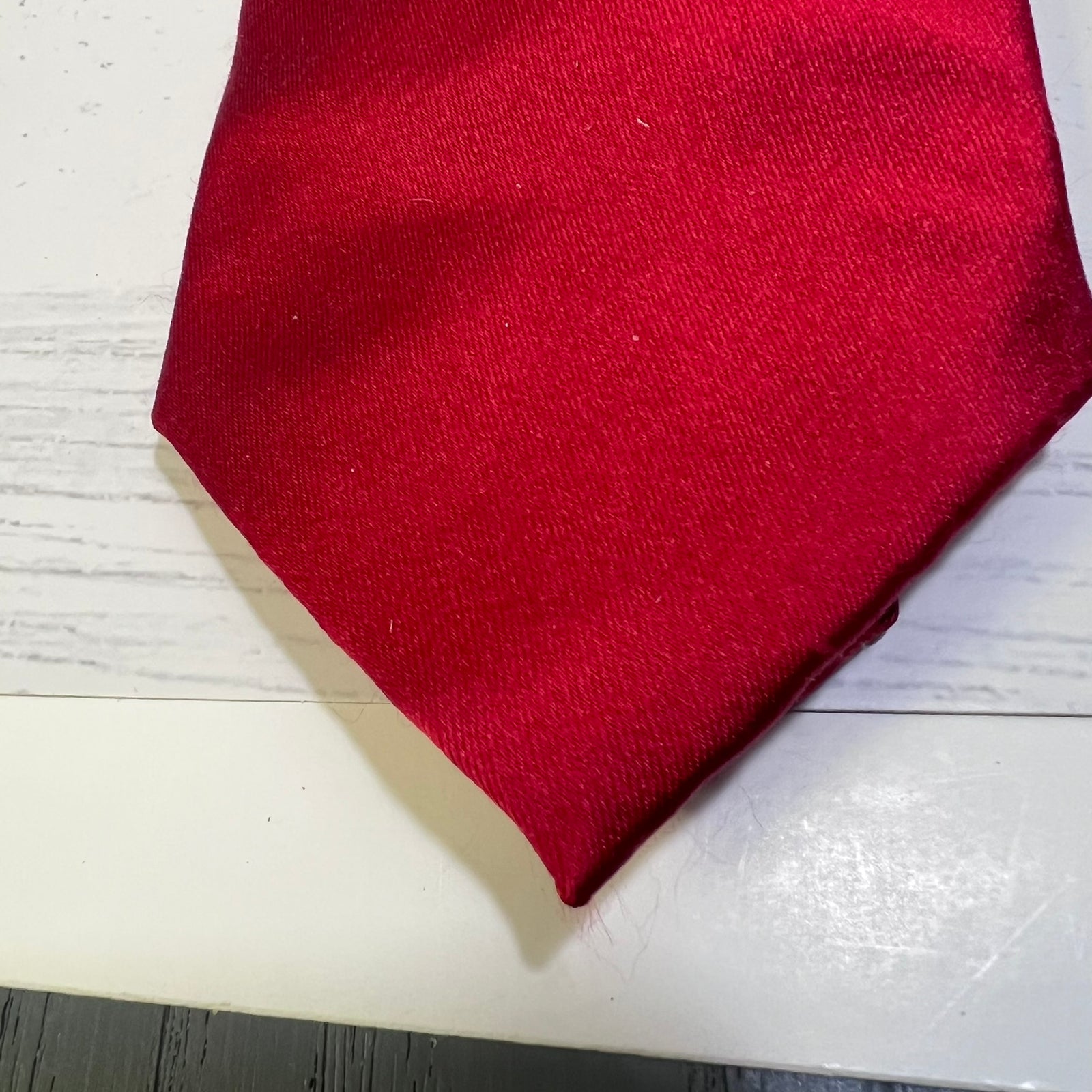 A close-up of a folded red fabric item, likely a scarf or necktie, showing its woven texture on a white wooden surface.