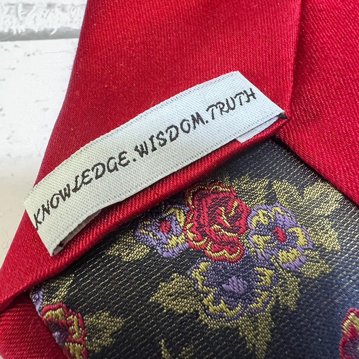 Close-up of a red necktie collar with a white fabric label reading 'KNOWLEDGE.WISDOM.