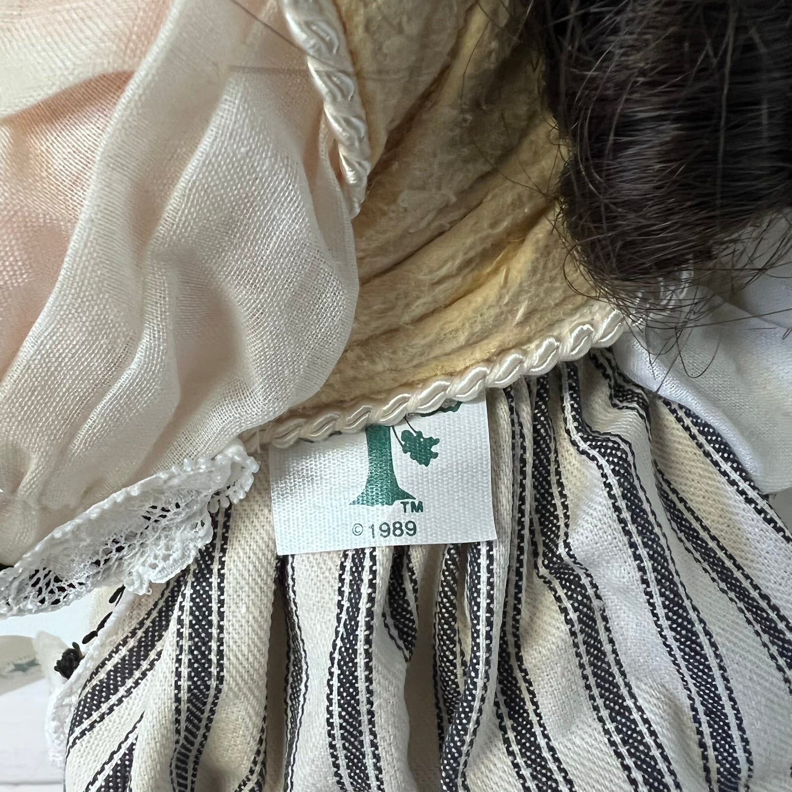 Close-up of a vintage striped garment with a white fabric label reading 'PONY 1989' and a green tree logo, showing cream and black stripes with lace trim.