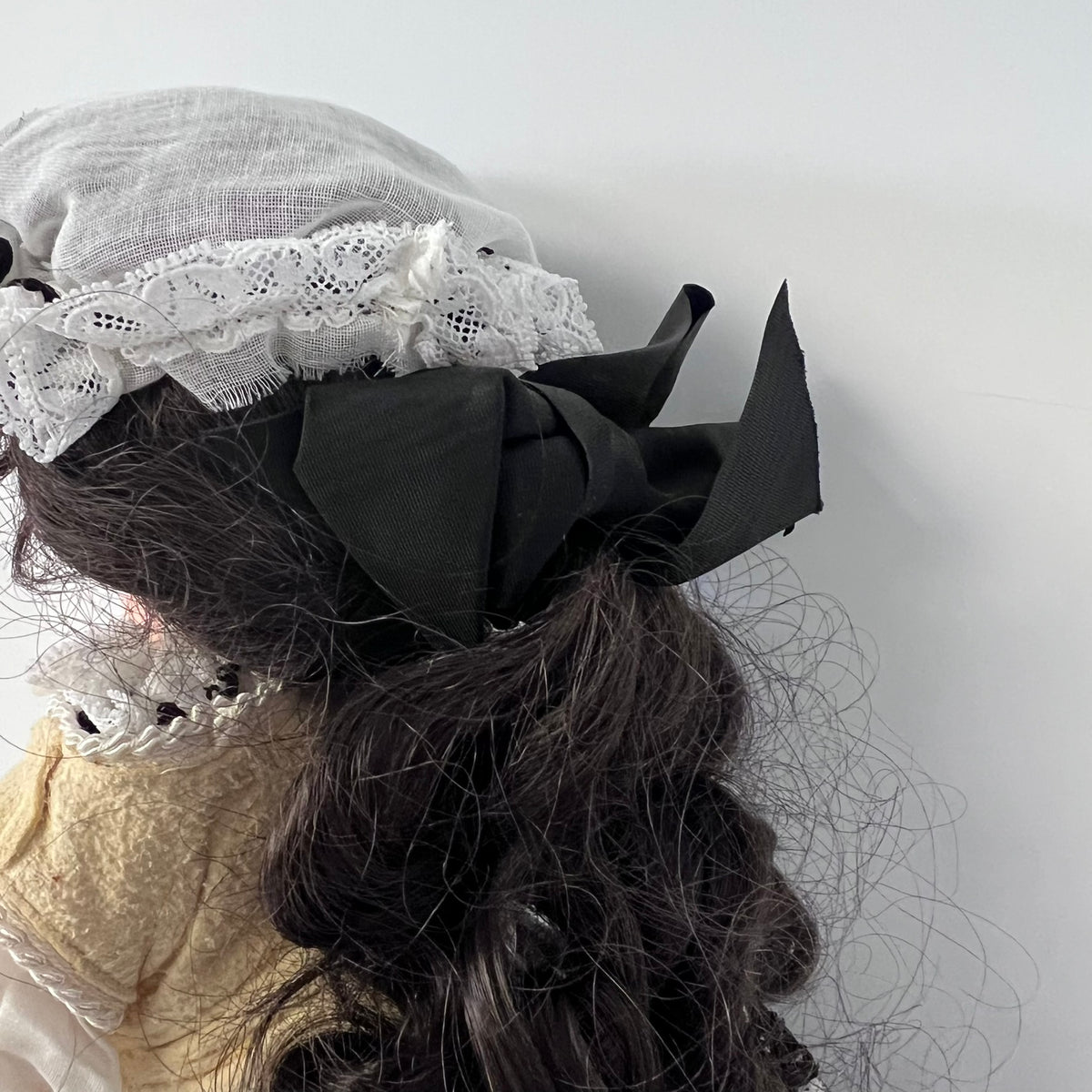 A close-up of a person's dark wavy hair styled with a large black fabric bow and a white lace headband against a plain light gray background.