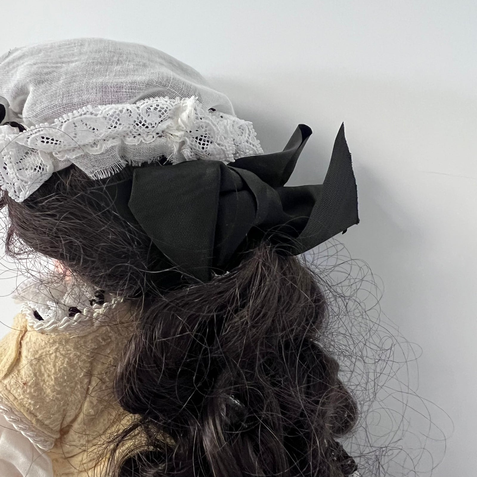 A close-up of a person's dark wavy hair styled with a large black fabric bow and a white lace headband against a plain light gray background.