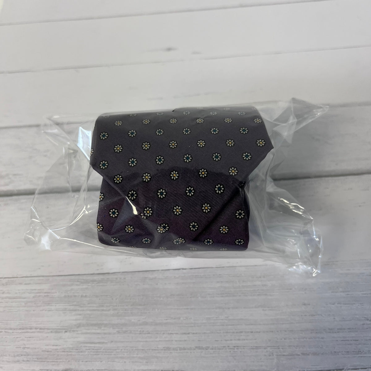 Dark patterned tie in clear plastic packaging on a light wooden surface