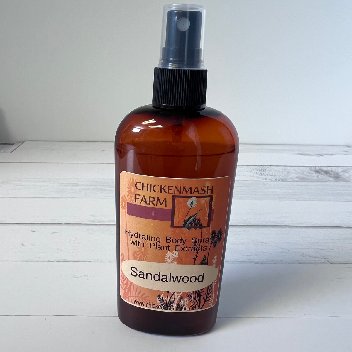 Brown spray bottle labeled 'Chickenmash Farm Sandalwood' on a white wooden surface.