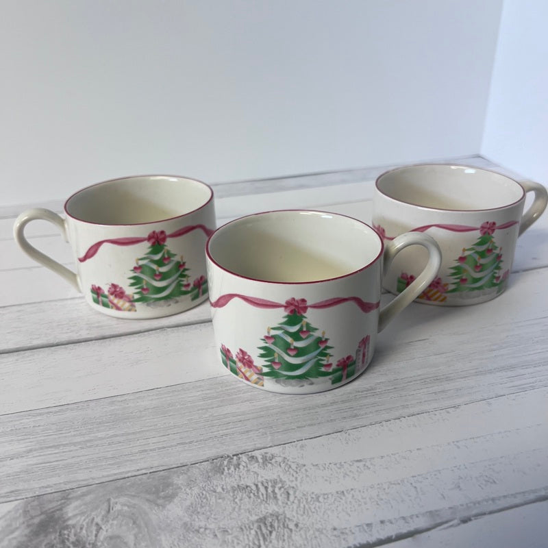 Three ceramic mugs with Christmas tree design on a white wooden surface