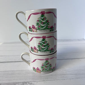 Stack of three Christmas-themed mugs with tree and gift designs on a white wooden surface.