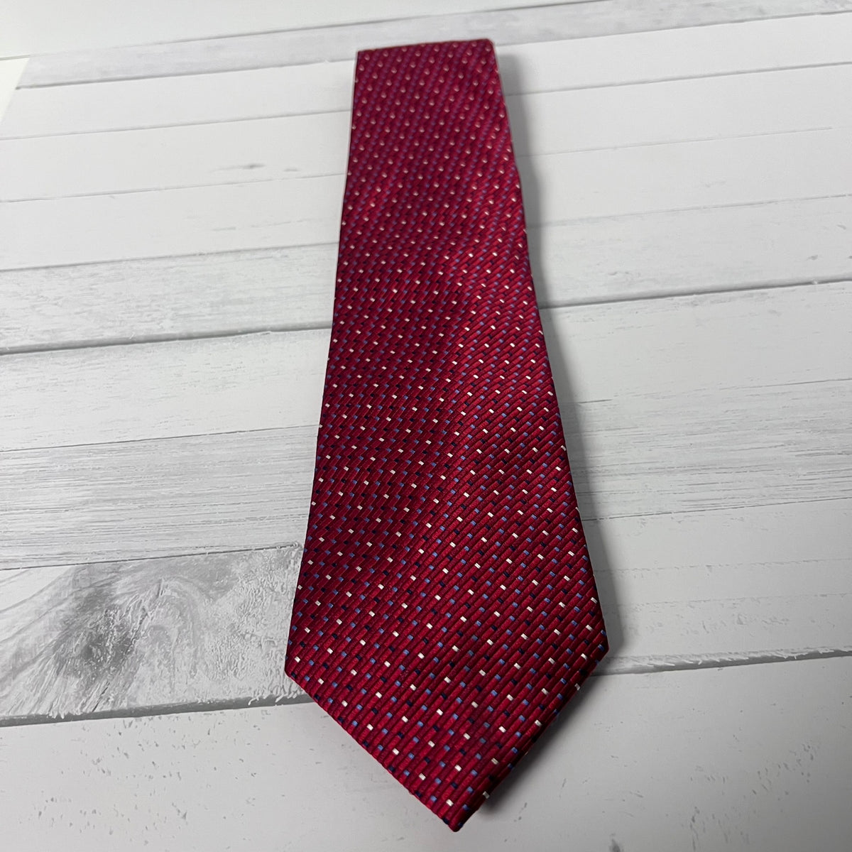 A red necktie with a small white geometric pattern, laid flat on a white wooden plank surface.