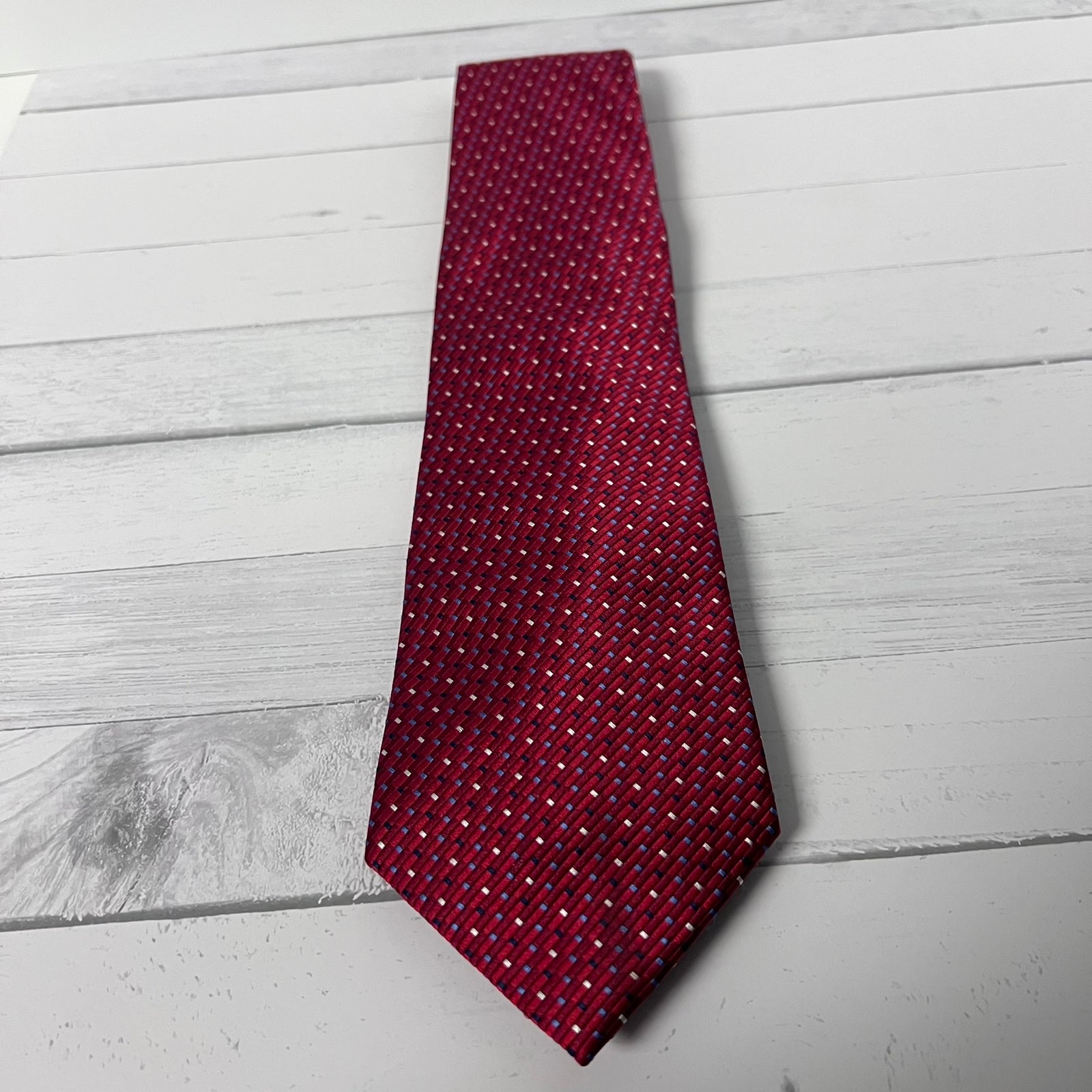 A red necktie with a small white geometric pattern, laid flat on a white wooden plank surface.