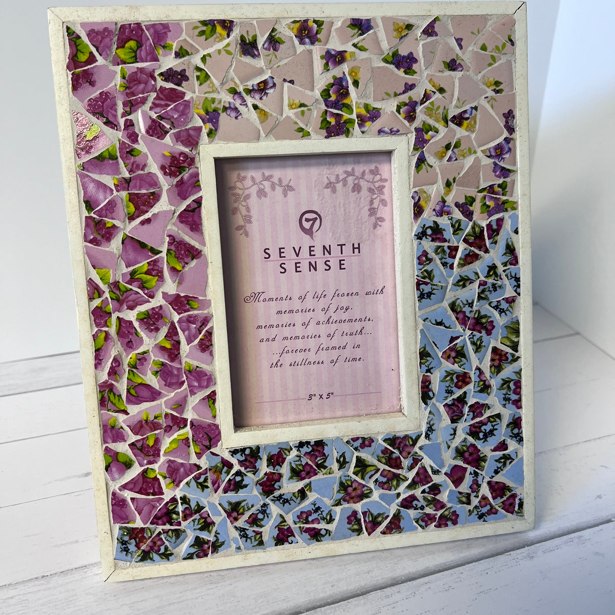 A square mosaic picture frame with a floral design, featuring purple and pink flower pieces on a light background. The center has a white mat and a placeholder insert card that reads 'SEVENTH SENSE'.